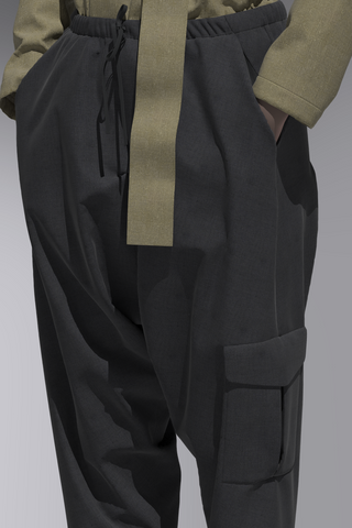 Zoomed in view of 3D garment- dark grey drawstring, elastic waist pant with drop crotch and cargo pocket. Top is light olive, tucked into pant with belt hanging down. Avatar's hands are in the pant pockets.